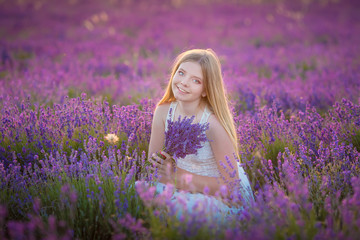 Smiling beautiful blond lady model on lavender field enjoy summer day wearing airy whit dress with bouquet of flowers.