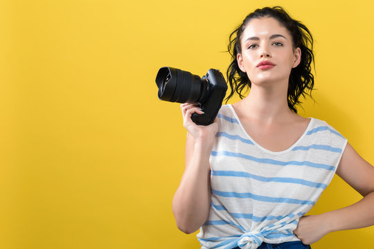 Young woman with a professional digital SLR camera on a yellow background