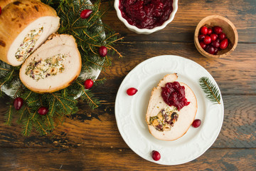 Stuffed  turkey breast roll with cranberry sauce on white plate on rustic wooden table, top view