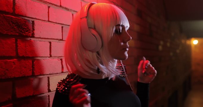 Sexy unusual girl in white wig listening to music using headphones, red light corridor