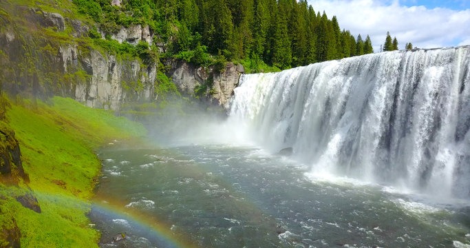 Mesa Falls, Idaho, USA - Wide Waterfalls Surrounded By Green Pine Trees With A Rainbow