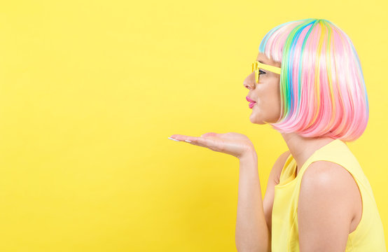 Woman in a colorful wig blowing a kiss on a yellow background