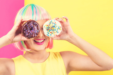 Beautiful woman in a colorful wig with doughnuts on a split yellow and pink background