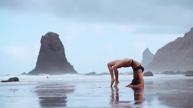 Girl gymnast on the beach makes a wheel and becomes a pose bridge standing on his hands and feet flexing in the back on the ocean