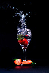  Strawberry splashing into a wine glass, transparent liquid isolated on black background.
