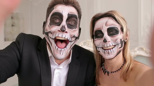 Portrait of scary people with a terrible makeup in the form of a skull or dead people. Couple very scared laughing showing teeth. Outfit for halloween. A couple of zombies take selfies on Halloween.