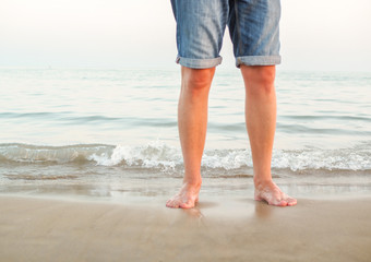 Mann am Strand am Meer steht mit nackten Beinen im Wasser