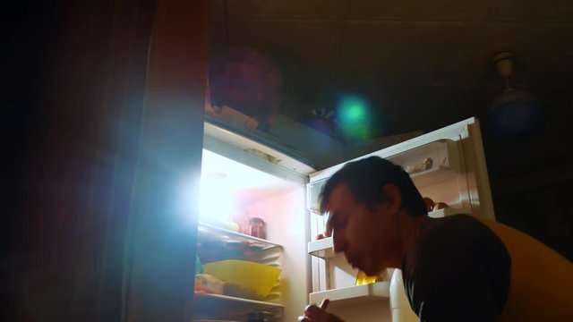 man eats hunger and gluttony from the refrigerator at night. man looks into the fridge at night. gluttony lifestyle overweight overeating concept