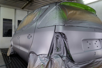 Full painting of a silver car in the body of a hatchback, some parts of which are protected by paper from splashes of paint droplets in a vehicle body repair workshop with a special box and equipment