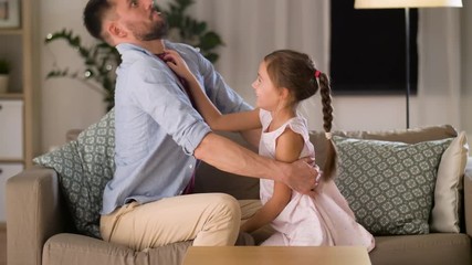 family, childhood and fatherhood concept - happy father and little daughter tickling and having fun on sofa at home