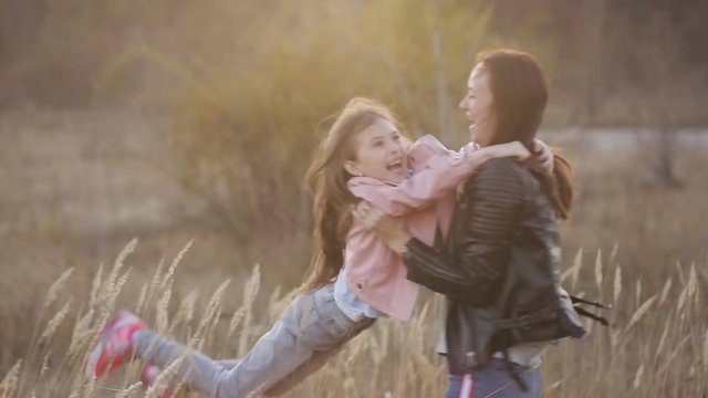A joyful mother whirls her little daughter, laughs and hugs her in the middle of the steppe