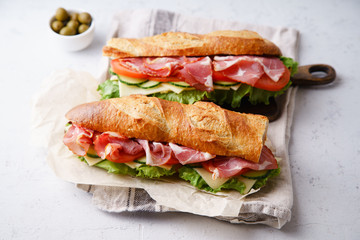 Side view of two fresh baguette sandwiches bahn-mi styled. Ham, sliced cheese, tomatoes and fresh lettuce, styled on concrete background.