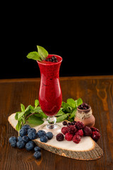 Glass of red raspberry fresh shake decorated with mint and blueberry at a wooden table isolated at black background.