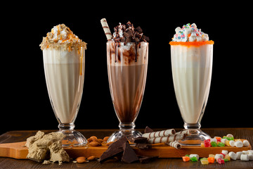 Three sweet milkshakes with chocolate, marshmallow, halva and whipped cream at a wooden board on a...