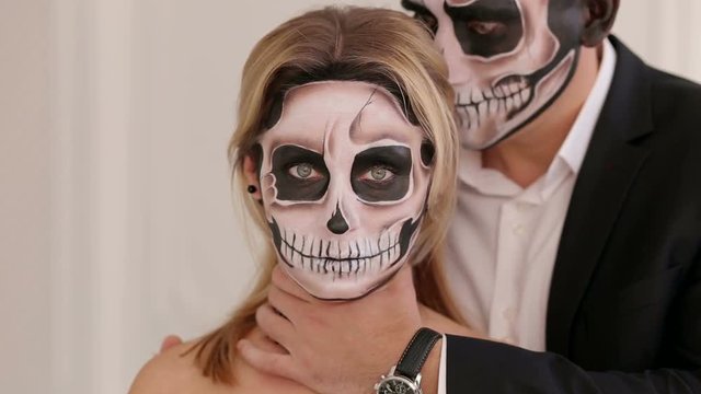 Close-up portrait of a creepy girl with makeup in the form of a skull, a man holding her neck trying to strangle. Women dressed in costume cosplay horror zombies or ghost on Halloween festival.