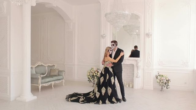 A man and a woman in a dress and costume with a creepy Halloween makeup, they stand cuddling in a beautiful white vintage room of an ancient castle. Couple of zombies. Halloween face art.