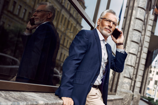Successful businessman. Serious senior man in casual suit talking on the phone while walking outdoors