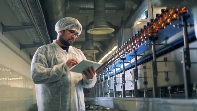 Bottled beer is moving along the conveyor under supervision of a male worker