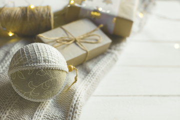 Fototapeta na wymiar Christmas New Year presents packaging. Gift boxes in craft paper tied with twine hand made fabric ornament ball white knitted sweater on wood table by window. Cozy magic winter evening warm colors