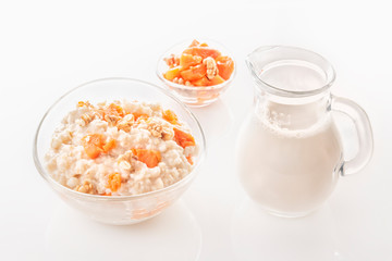 Oatmeal with pumpkin and nuts in a glass plate and a jug with milk on a white background. Close-up