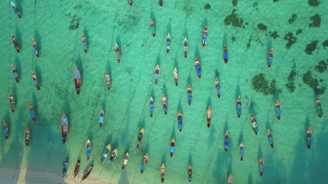 Top of traditional Thai boats, white sand beach, beautiful clear emerald sea, seen from camera down forward moving high aerial drone view on tropical island, Ko Lipe, Thailand.