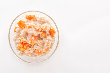Fototapeta na wymiar Oatmeal with pumpkin and nuts in a glass plate on a white background. Copy space. Top view