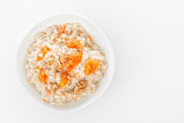 Fototapeta na wymiar Oatmeal with pumpkin and nuts in a white plate on a white background. View from above. Copy space. Close-up