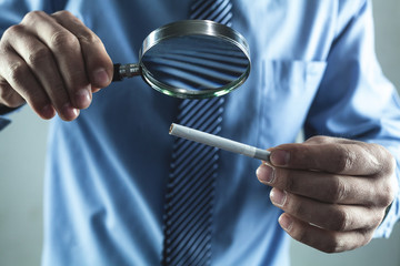 Man holding magnifying glass with cigarette.