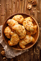 Croissants with shortcrust pastry with rose jam filling sprinkled with nuts and sesame seeds on a wooden plate, top view. Delicious homemade dessert