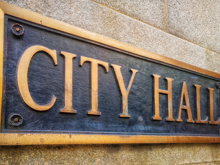 Exterior sign that reads "City Hall" in brass letters. Close up. Graphic resource.