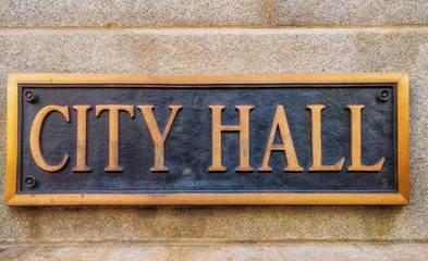 Exterior sign that reads "City Hall" in brass letters.