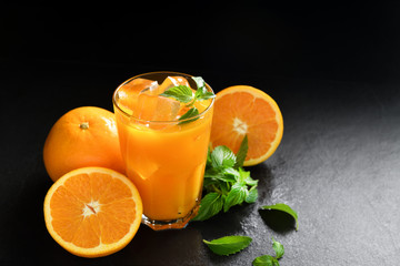Fresh orange juice in glass surrounded by oranges on black background