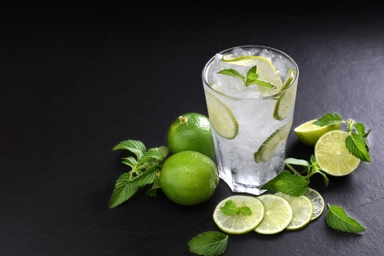 Fresh lime soda in glass drink with sliced lime on black background