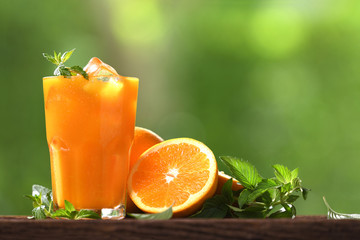 Fresh orange juice in glass with sliced orange on wood and nature background - obrazy, fototapety, plakaty