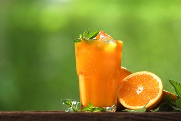 Fresh orange juice in glass with sliced orange on wood and nature background