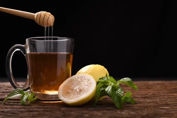 Crédence de cuisine en verre imprimé Theé Thé chaud au citron et au miel en verre à la menthe et au citron tranché sur table en bois et fond noir