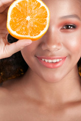 Young smiling black girl with clean perfect skin with orange close-up
