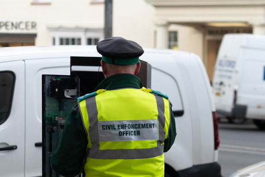 civil enforcement officer traffic warden tries to fix broken parking meter in busy high street
