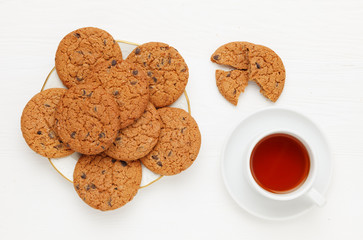 Oatmeal cookie with chocolate chip on a plate and a Cup of tea on a white wooden background