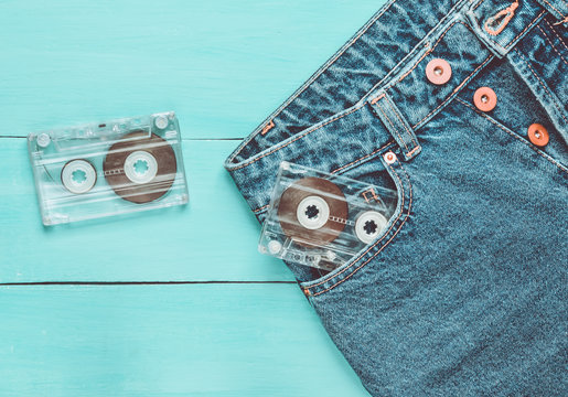 Two audio cassettes in a jeans pocket on a blue wooden surface. Media technology from the 80s.