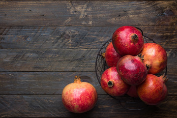 Ripe juicy organic bright red pomegranates in metal wicker basket on reclaimed plank barn wood background. Fall produce harvest vitamins abundance concept. Rosh Hashanah holiday.