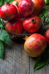 Ripe juicy organic bright red pomegranates in metal wicker basket with branches green leaves on plank barn wood background. Fall produce harvest vitamins abundance concept. Rosh Hashanah holiday