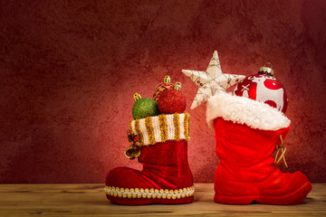 Zwei Nikolaus Stiefel mit Christbaumkugeln vor einer roten Wand