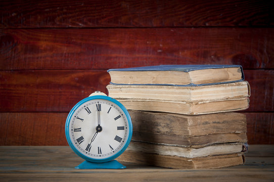 stack of books and alarm clock on it on wooden table.