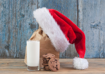 Obraz na płótnie Canvas Milk and cookies for Santa Claus and Santa's hat over wooden background.