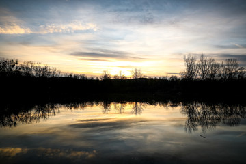 Obraz premium The lake during sunset looking at the water and the trees on the other side of the shadows.