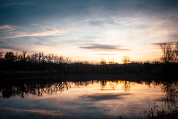 Obraz premium The lake during sunset looking at the water and the trees on the other side of the shadows.
