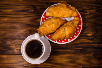 Cup of dark coffee and croissants on wooden table. Top view