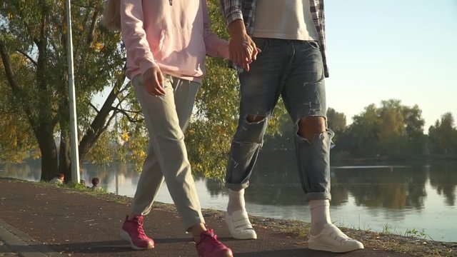 Young man and lady walk in the park holding hands