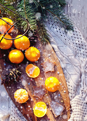 Fototapeta na wymiar Tangerines waffle cookies fir tree brunches, pine cones on wooden kitchen board in rustic style on white wooden table background and gray knitted cloth. Christmas food decorations. Flat lay copy space